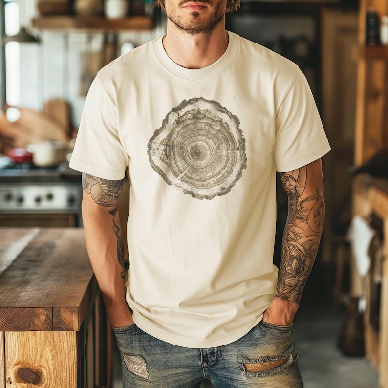 May include: A cream colored t-shirt with a graphic print of a tree ring. The t-shirt has short sleeves and a crew neck.
