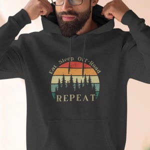 May include: A dark grey hooded sweatshirt with a vintage-style graphic that reads "Eat Sleep Off-Road Repeat" with a sunset and pine trees.