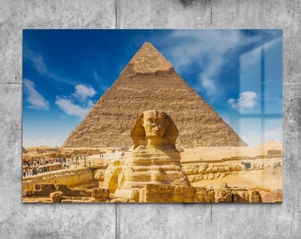 May include: A framed print featuring the Great Sphinx of Giza and the Great Pyramid against a bright blue sky with scattered clouds. The Sphinx is a large limestone statue with the body of a lion and the head of a human. The pyramid is in the background.