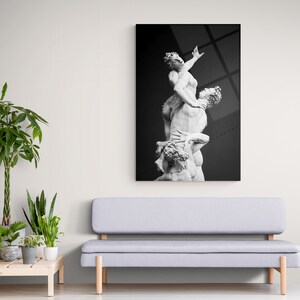 Pu&ograve; includere: Fotografia in bianco e nero di una scultura di tre figure intrecciate. La scultura &egrave; in marmo bianco e si trova su uno sfondo scuro.