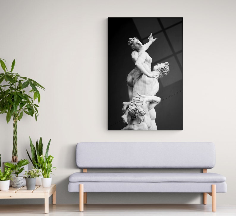Pu&ograve; includere: Fotografia in bianco e nero di una scultura di tre figure intrecciate. La scultura &egrave; in marmo bianco e si trova su uno sfondo scuro.