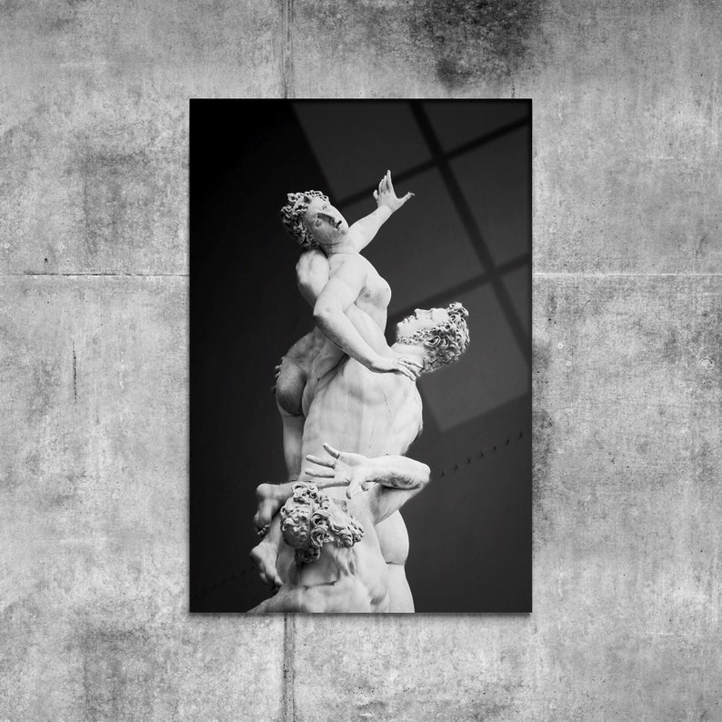 Pu&ograve; includere: Fotografia in bianco e nero di una scultura che rappresenta tre figure in una posa dinamica. Le figure sono nude e sembrano intrecciarsi, creando un senso di movimento e tensione.