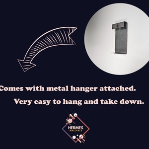 Pu&ograve; includere: Primo piano di un muro bianco con un gancio di metallo attaccato. Il gancio &egrave; progettato per facilitare l'appendimento e la rimozione di un'immagine o di altri decori da parete.