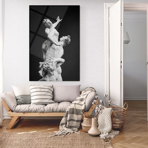 Pu&ograve; includere: Una fotografia in bianco e nero di una scultura che rappresenta tre figure in una posa drammatica. La scultura &egrave; esposta su una parete in un ambiente di soggiorno moderno.