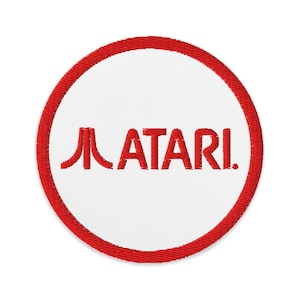May include: A red and white embroidered patch with the Atari logo and the word "ATARI" in red.