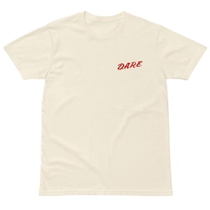 Puede incluir: Camiseta crema de manga corta con la palabra "DARE" bordada en rojo en la parte superior izquierda del pecho. La camiseta tiene cuello redondo y un corte relajado, adecuada para ropa informal.