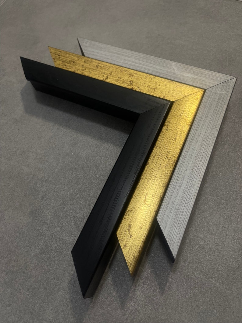 May include: Three picture frames, one black, one gold, and one gray, are stacked on top of each other. The frames are all the same size and shape, and they are all made of wood.