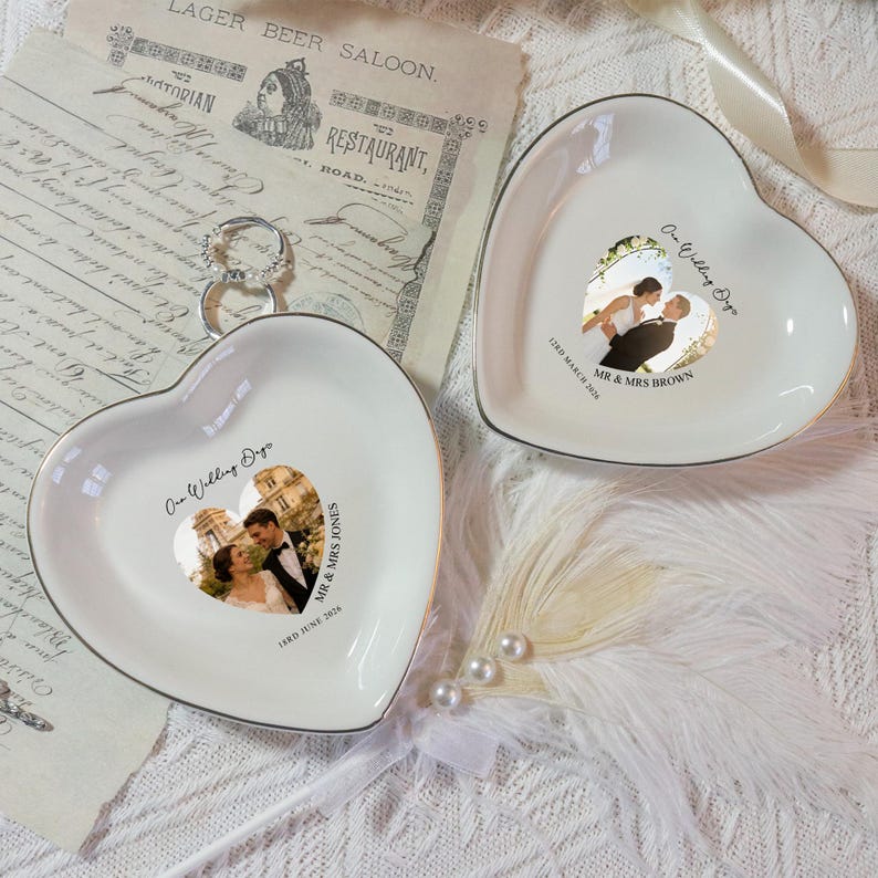 May include: Two heart-shaped ceramic ring dishes with gold trim. Each dish features a wedding photo and the text "One Wedding Day" and the wedding date. One dish has "Mr & Mrs Brown" and the other has "Mr & Mrs Jones".