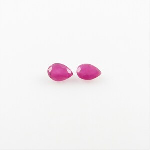May include: Two pear-shaped pink gemstones, likely rubies, on a white background.