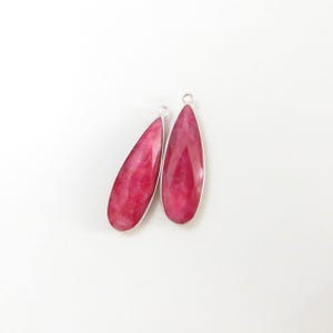 May include: Two teardrop-shaped pink gemstone pendants with silver settings. The gemstones have a marbled pattern.