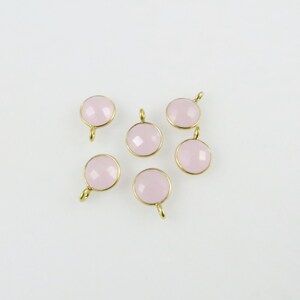 May include: Six pink gemstone charms with gold settings. The charms are round and have a faceted design.