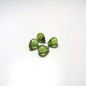 Peut inclure: Quatre pierres précieuses vertes claires, taillées en forme de poire, sont disposées sur une surface blanche. Les pierres ont une qualité translucide, avec des facettes internes visibles qui captent la lumière. L'effet général est d'une beauté délicate.