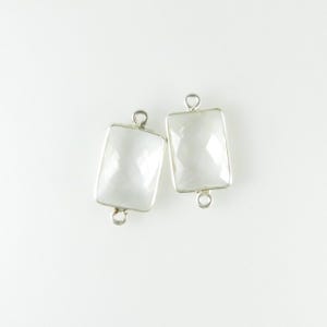 Puede incluir: Dos conectores rectangulares de gemas blancas facetadas, con marcos y bucles de metal plateado. Las gemas tienen un brillo sutil y nacarado. Diseñados para la creación de joyas.