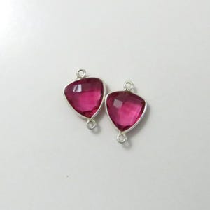 Puede incluir: Dos colgantes de forma triangular plateados con gemas facetadas de color rosa. Los colgantes tienen un bucle a cada lado para sujetarlos a una cadena o cordón.