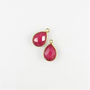 May include: Two teardrop-shaped ruby red gemstone pendants with gold-toned metal settings and jump rings.