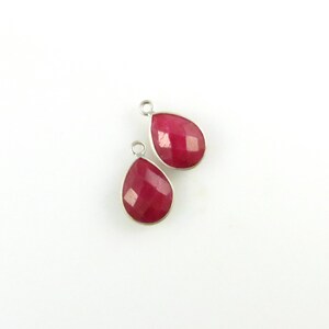 May include: Two red gemstone teardrop pendants with silver settings. The pendants are faceted and have a shiny finish.
