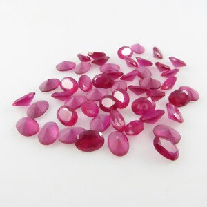 Puede incluir: Un montón de piedras preciosas de rubí talladas en forma ovalada. Los rubíes son de color rosa intenso y tienen un alto brillo.