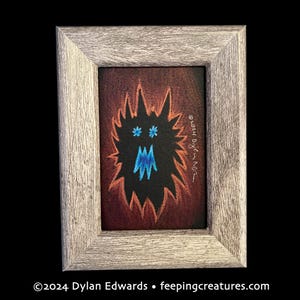 Può includere: Opera d'arte incorniciata raffigurante un mostro stilizzato con corpo nero e contorno arancione. Il mostro ha occhi blu e bocca blu. L'opera è in una cornice di legno grigio. Il testo "©2024 Dylan Edwards • feepingcreatures.com" è in basso.