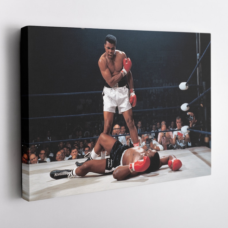 Peut inclure: Une photo en noir et blanc d'un match de boxe. Un boxeur en short blanc se tient au-dessus d'un boxeur allong&eacute; sur le sol. Le boxeur au sol porte des gants de boxe rouges. La photo a &eacute;t&eacute; prise dans un ring de boxe avec une foule de personnes regardant en arri&egrave;re-plan.