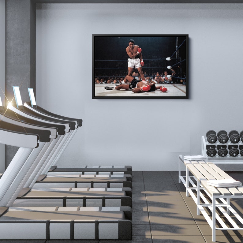 Peut inclure: Une photo en noir et blanc d'un match de boxe. Le boxeur de gauche lance un coup de poing, tandis que le boxeur de droite est au sol. La photo est encadr&eacute;e et accroch&eacute;e au mur d'une salle de sport.