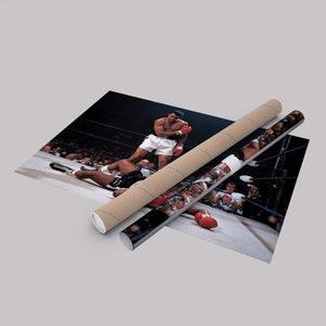 Peut inclure: Une photo en noir et blanc d'un match de boxe. Un boxeur portant des gants rouges se tient au-dessus d'un boxeur tomb&eacute;. Le boxeur tomb&eacute; est allong&eacute; sur le sol du ring de boxe. La photo est prise d'un angle &eacute;lev&eacute;, regardant vers le bas sur le ring.