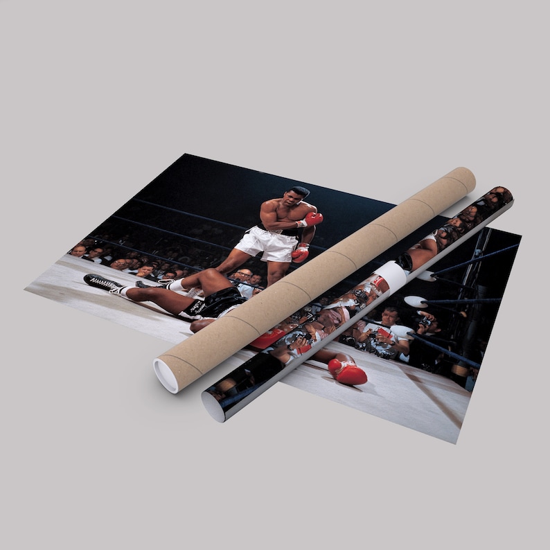 Peut inclure: Une photo en noir et blanc d'un match de boxe. Un boxeur portant des gants rouges se tient au-dessus d'un boxeur tomb&eacute;. Le boxeur tomb&eacute; est allong&eacute; sur le sol du ring de boxe. La photo est prise d'un angle &eacute;lev&eacute;, regardant vers le bas sur le ring.