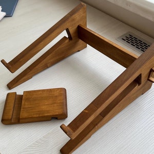 Op de afbeelding: Een houten laptopstandaard met een aparte telefoonstandaard. De standaard is gemaakt van natuurlijk hout en heeft een lichtbruine kleur.
