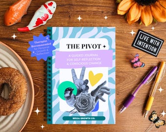 May include: A spiral-bound journal titled "The Pivot" with a blue and white cover, featuring a collage of images. The journal is accompanied by pens, decorative butterflies, and a patch that reads "Live With Intention". A donut and fish figurines are also present.