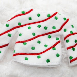 May include: White elf sweater with red and green candy cane stripes and green squares.