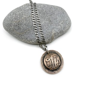 May include: A silver necklace with a circular pendant. The pendant has the word "Otis" in a decorative script, with a globe design. The necklace is displayed on a grey stone. The chain is silver.