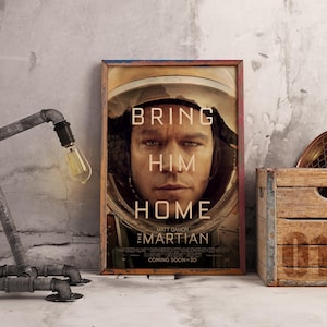 May include: Framed movie poster for "The Martian" featuring Matt Damon. The poster has a distressed wooden frame and shows Damon's face inside a space helmet with the words "BRING HIM HOME" in large letters. The movie title and "COMING SOON 3D" are also visible.
