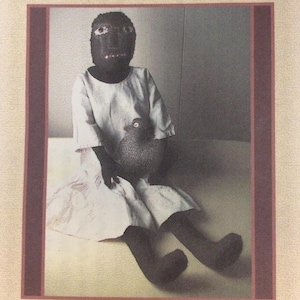 May include: A craft pattern titled with Rooster No. 00-006A, featuring a Primitive Wool-Hooked 28-inch Doll Pattern by Laetitia Bachleda. The image shows a dark-skinned doll wearing a white dress and holding a textured gray bird figure.