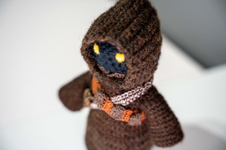Peut inclure: Un jouet en peluche crochet&eacute; marron avec une robe &agrave; capuche et des yeux jaunes. Le jouet est fait de fil doux et a un visage d&eacute;taill&eacute;.