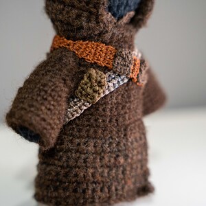 Peut inclure: Un jouet en peluche crochet&eacute; marron avec une ceinture crochet&eacute; marron, orange et verte. Le jouet porte une robe &agrave; capuche marron.