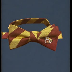 May include: A striped bow tie in maroon and gold, featuring a crest with the letters "K" and "L". The bow tie has a classic shape and is set against a dark blue background. The stripes are evenly spaced.