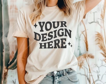 May include: A beige t-shirt with the text "YOUR DESIGN HERE" in black lettering with small stars on either side of the text.