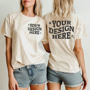 以下が含まれることがあります： 2人ともクリーム色のTシャツを着ています。Tシャツの前と後ろには「YOUR DESIGN HERE」という文字が印刷されています。Tシャツはゆったりとしたシルエットで、袖は短いです。
