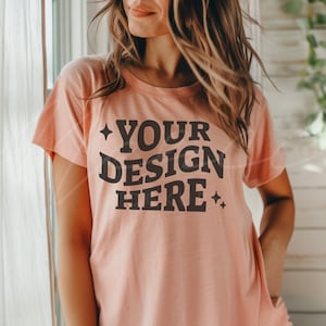 May include: A peach-colored t-shirt with short sleeves and a crew neck. The shirt has the text "YOUR DESIGN HERE" printed in black on the front.