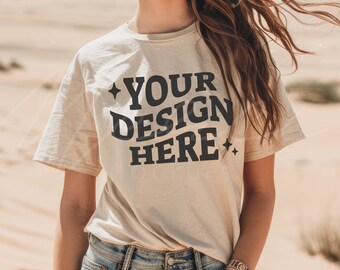 May include: A woman wearing a beige t-shirt with the text "YOUR DESIGN HERE" printed on it. She is standing in a desert setting.