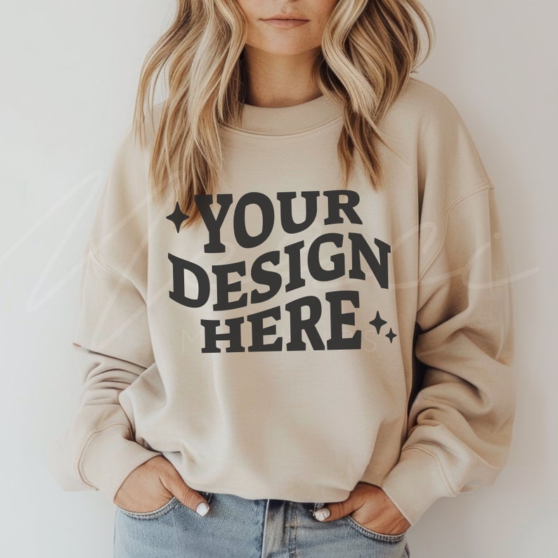 May include: A beige sweatshirt with the text "YOUR DESIGN HERE" in black lettering. The sweatshirt has a relaxed fit and long sleeves.