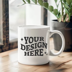 May include: White ceramic mug with a black design that says "YOUR DESIGN HERE" in a retro font. The mug is sitting on a wooden table.