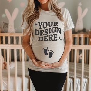 Könnte beinhalten: Ein weißes T-Shirt mit dem Text "YOUR DESIGN HERE" und einem Paar Babyfüßen auf der Vorderseite. Das Shirt wird von einer schwangeren Person getragen.