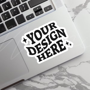 May include: A white laptop with a black keyboard and a black and white sticker that says "YOUR DESIGN HERE" with two stars on either side of the text.