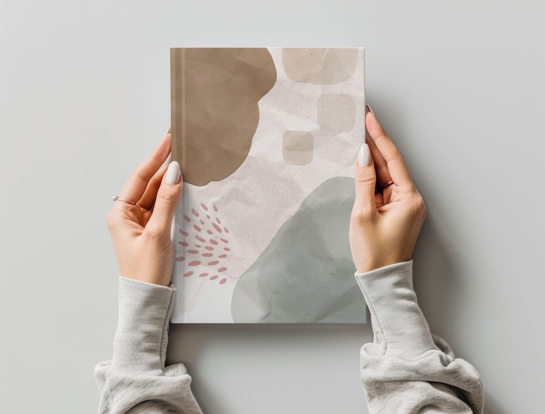 May include: A notebook with an abstract design featuring brown, gray, and pink watercolor shapes. The notebook has a textured paper cover.