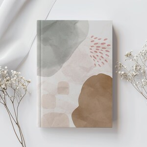 May include: A notebook with an abstract design featuring watercolour-like shapes in shades of grey, brown, and pink. The cover has a textured look and feel.