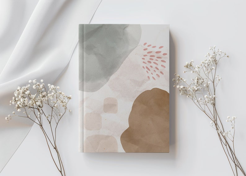 May include: A notebook with an abstract design featuring watercolour-like shapes in shades of grey, brown, and pink. The cover has a textured look and feel.