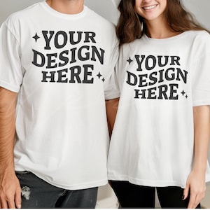 Puede incluir: Dos camisetas blancas con el texto "Your Design Here" impreso en ellas. Las camisetas las llevan puestas dos personas que están de pie una al lado de la otra.