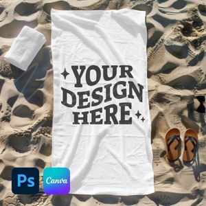 Op de afbeelding: Wit strandlaken met de tekst "YOUR DESIGN HERE" in zwarte letters op een zandstrand achtergrond.