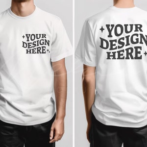 以下が含まれることがあります： 白い半袖のクルーネックTシャツ。シャツの前側は空白です。シャツの後ろ側には黒い文字で「YOUR DESIGN HERE」と印刷されています。