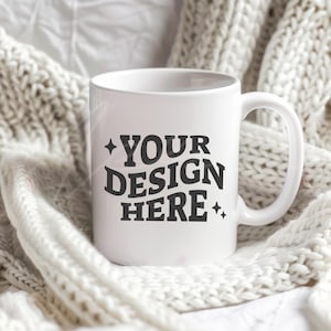 May include: White ceramic mug with a black design that says "YOUR DESIGN HERE" surrounded by small stars. The mug is sitting on a white knitted blanket.